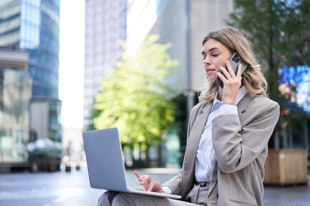 Бесплатное фото Деловая женщина проверяет схему и работает на ноутбуке, звонит кому-то по мобильному телефону, сидя на улице.