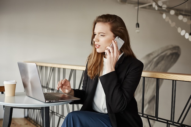 Бесплатное фото Деловая женщина, работающая в кафе, отвечает на звонки и смотрит на ноутбук