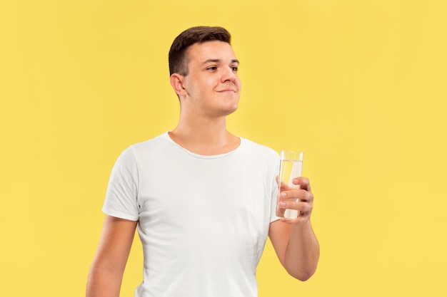 Free photo caucasian young man's half-length portrait on yellow studio background. beautiful male model in shirt. concept of human emotions, facial expression, sales, ad. enjoying drinking pure water.