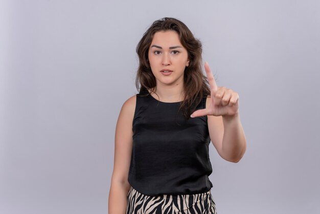 Free photo caucasian young woman wearing black undershirt her finger to up on white wall