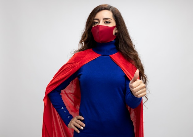 Бесплатное фото Уверенная кавказская девушка супергероя с красной накидкой в красной защитной маске