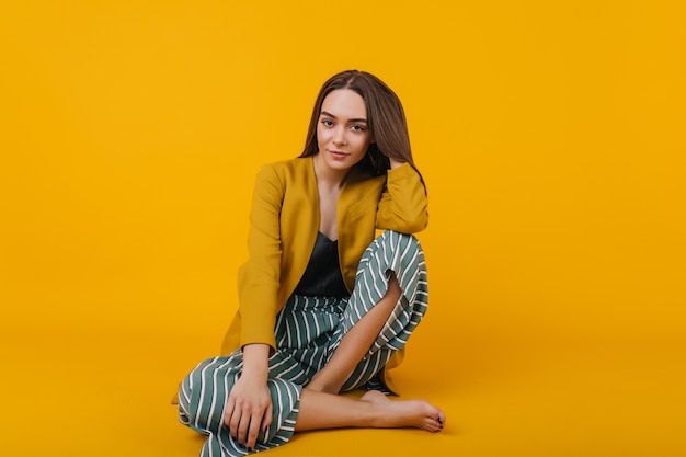 Free photo confident young lady in striped pants sitting. glad white girl wears yellow jacket.