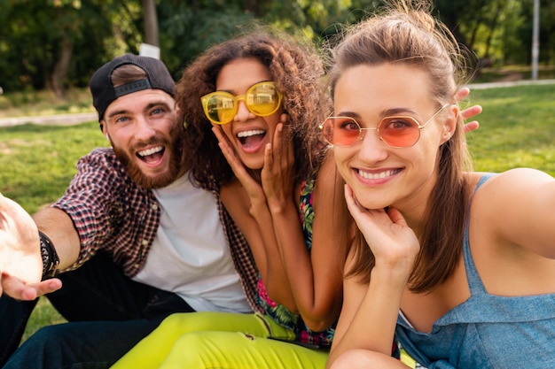 Бесплатное фото Красочная стильная счастливая молодая компания друзей, сидящих в парке, мужчины и женщины, весело проводящие время вместе