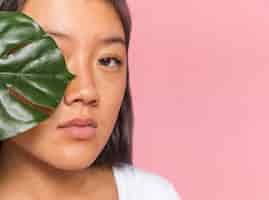 Free photo close-up woman covering her eye with monstera leaf