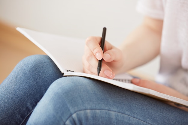 Бесплатное фото Крупным планом довольно молодая девушка-подросток сидит на полу и делает заметки в своем дневнике