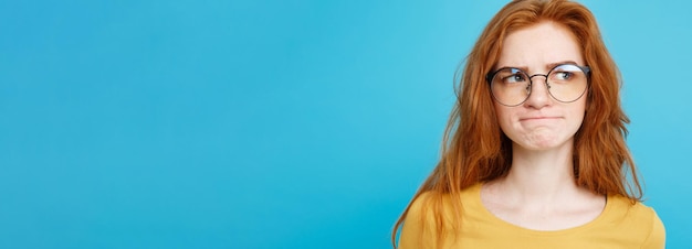 Бесплатное фото Крупным планом портрет молодой красивой привлекательной рыжеволосой девушки в очках, беспокоящейся о чем-то голубом