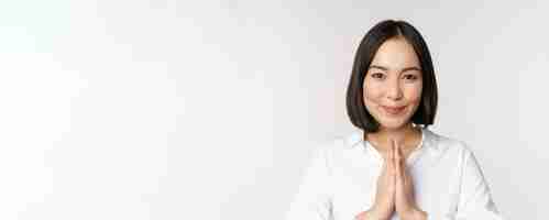 Бесплатное фото Крупный план портрета молодой японки, показывающей жест намасте спасибо аригато, стоящей на белом фоне