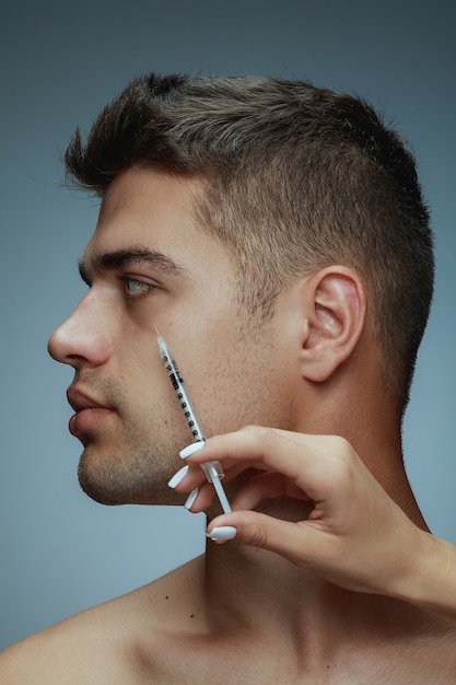 Free photo close-up profile portrait of young man isolated on grey studio background. filling surgery procedure. concept of men's health and beauty, cosmetology, self-care, body and skin care. anti-aging.