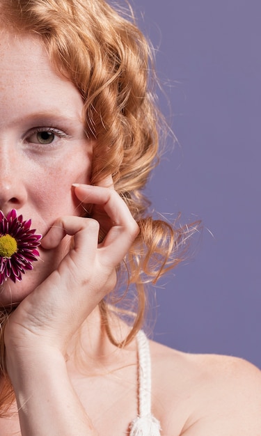 Close-up of redhead woman posing with a flower on her mouth