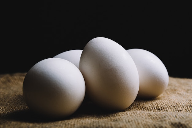 Closeup shot of four white eggs on a brown surface on a black wall
