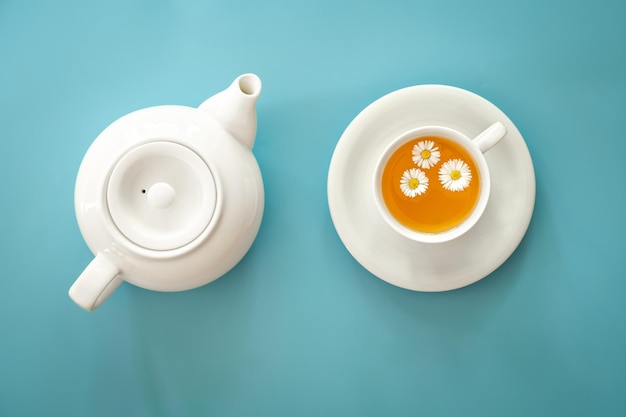 Free photo a cup of chamomile tea and a teapot on a blue background