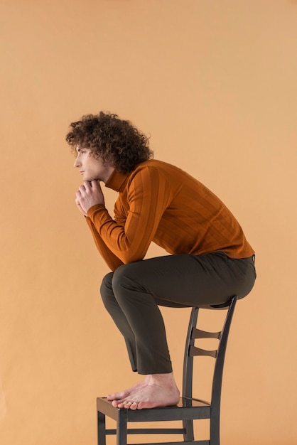 Free photo curly haired man with brown blouse posing on chair