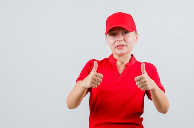 Free photo delivery woman in red t-shirt and cap showing thumbs up and looking satisfied