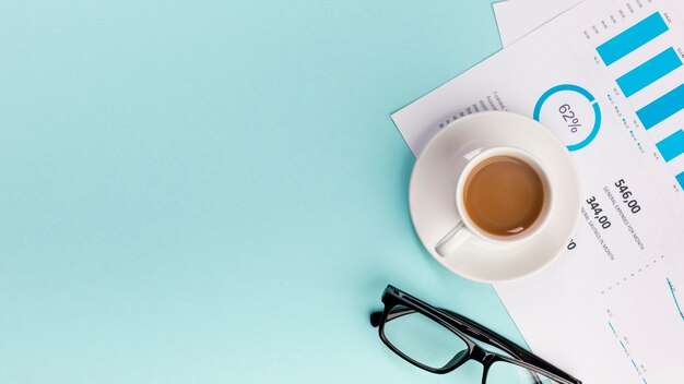 Поднятый вид кофейной чашки на бизнес-план бюджета и очки на синем фоне
