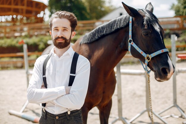 Элегантный мужчина стоит рядом с лошадью на ранчо