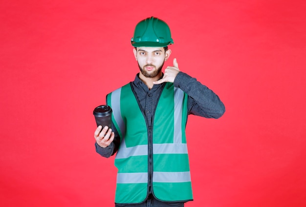 Бесплатное фото Инженер в зеленой форме и шлеме держит черную одноразовую чашку кофе.