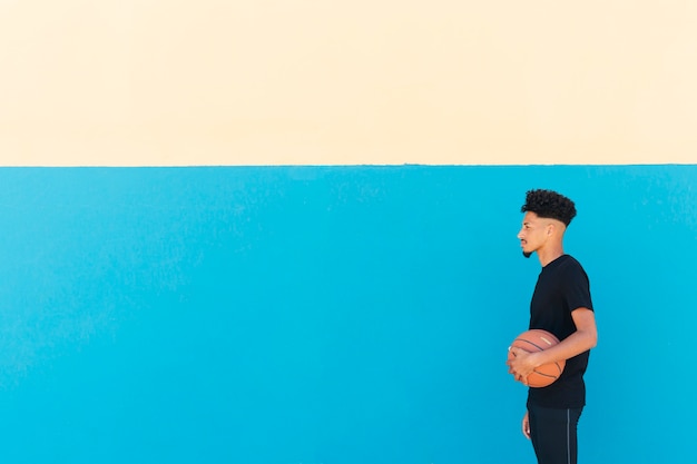 Этнический спортсмен с вьющимися волосами стоит с баскетболом