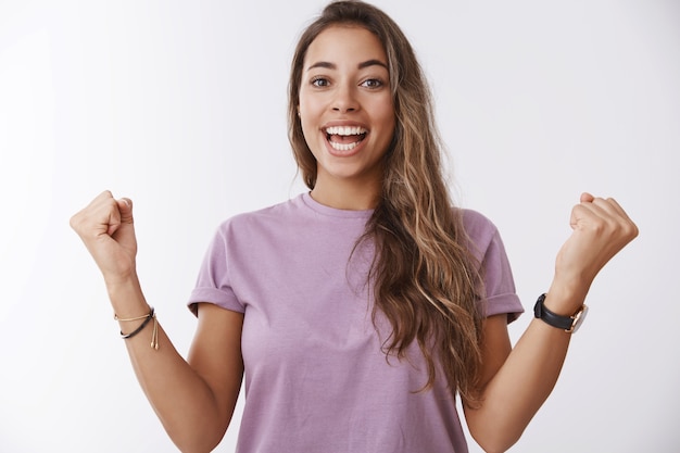 Free photo excited happy charming smiling woman, tanned curly hair, clenching fists joyfully celebrating accomplishment, victory successful cheer, hooray, joyful win, standing amused white wall
