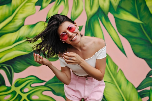 Бесплатное фото Возбужденная женщина с татуировкой смеется перед граффити привлекательная девушка, выражающая счастье в летний день