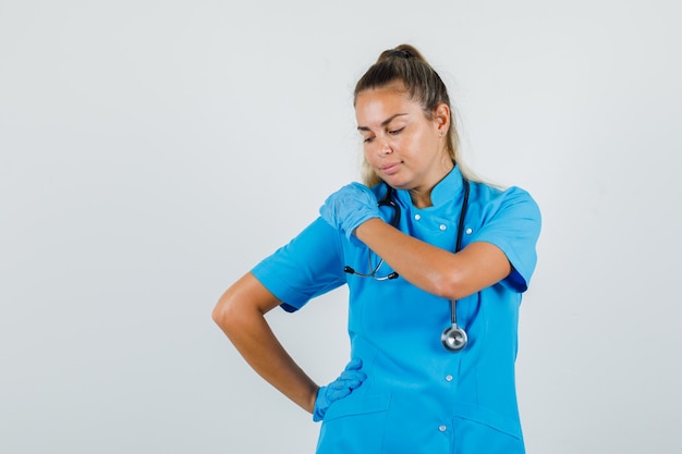 Free photo female doctor posing while hands on shoulder and waist in blue uniform