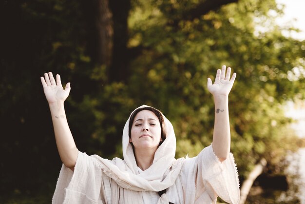 female wearing a biblical gown whit her hands up towards the sky