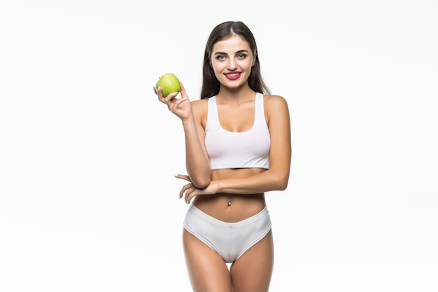 Бесплатное фото fit и спортивная девушка в белом нижнем белье. красивая и здоровая женщина ест зеленое яблоко над серой стеной.