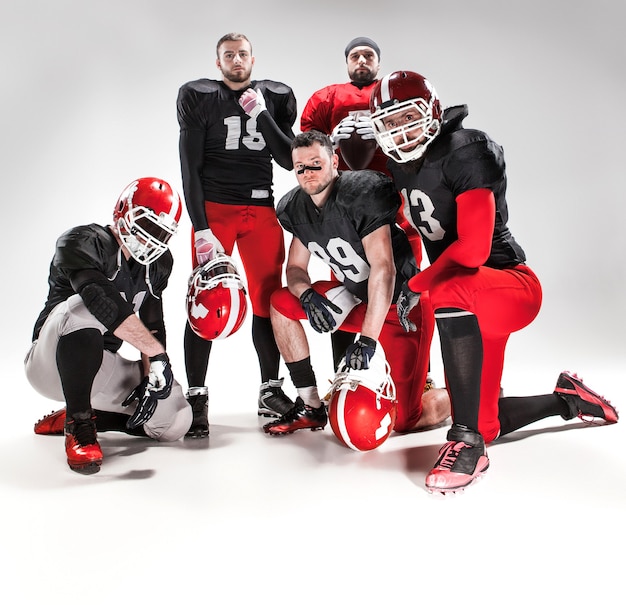 Free photo the five caucasian fitness men as american football players posing  full-length with a ball on white background