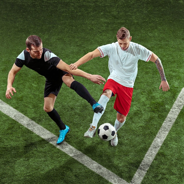 Футболист решает мяч над стеной из зеленой травы. Профессиональные футболисты мужского пола в движении на стадионе. Приспособьте прыгающих мужчин в действии, прыжке, движении в игре.