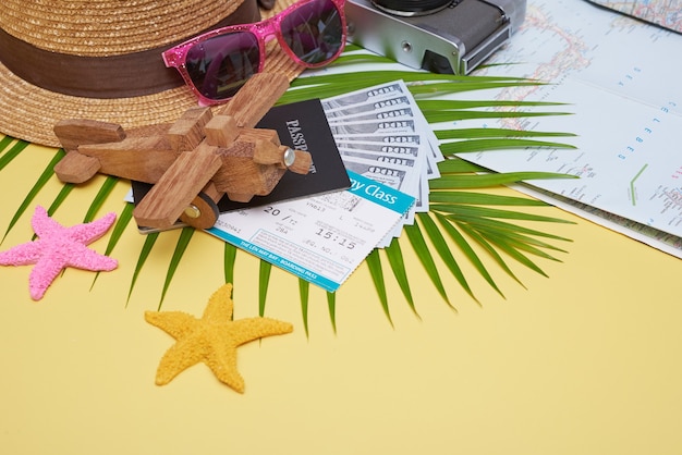 Free photo flat lay traveler accessories on yellow surface with palm leaf, camera, shoe, hat, passports, money, air tickets, airplanes and sunglasses. top view, travel or vacation concept.