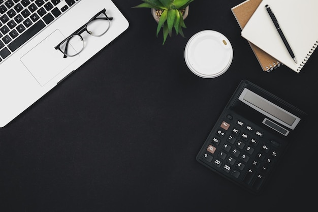 Бесплатное фото Плоский черный фон с чашкой кофе для ноутбука и калькулятором, вид сверху