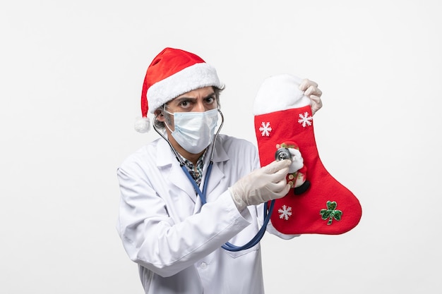Free photo front view male doctor observing holiday sock on the white wall covid virus holiday