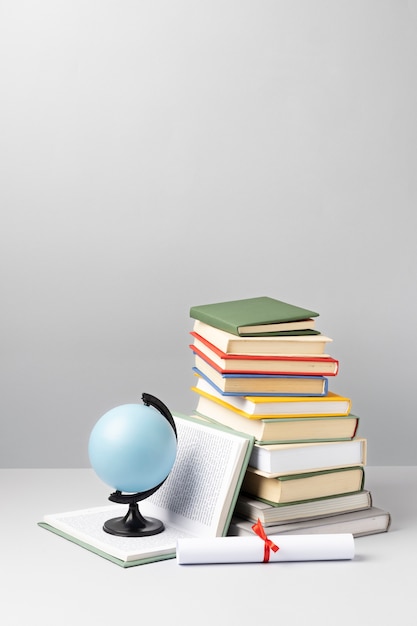 Бесплатное фото Вид спереди сложенных книг, диплома и земного шара с копией пространства на день образования