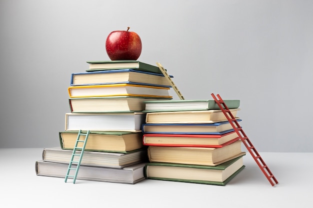 Бесплатное фото Вид спереди сложенных книг, лестниц и яблока с местом для копирования на день образования