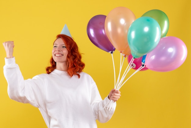 Бесплатное фото Вид спереди молодой женщины, держащей милые разноцветные шары на желтой стене