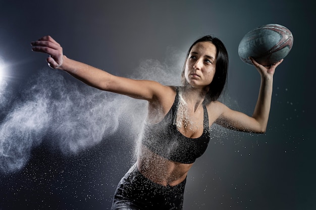 Foto gratuita vista frontale del giocatore di rugby femminile atletico che tiene palla con polvere