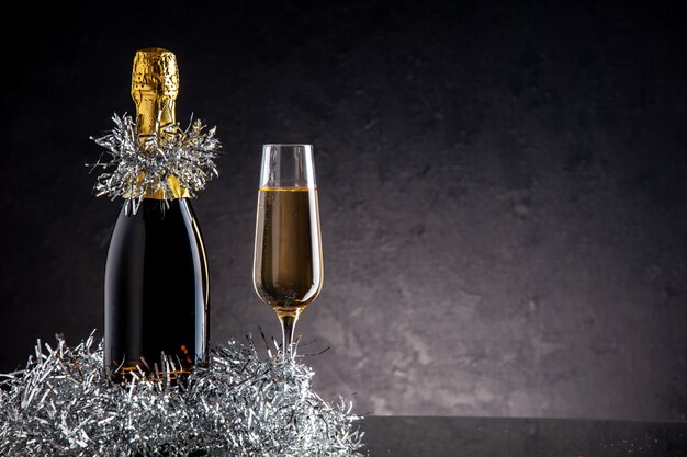 Бесплатное фото Шампанское в бутылке и бокал на темной поверхности, вид спереди