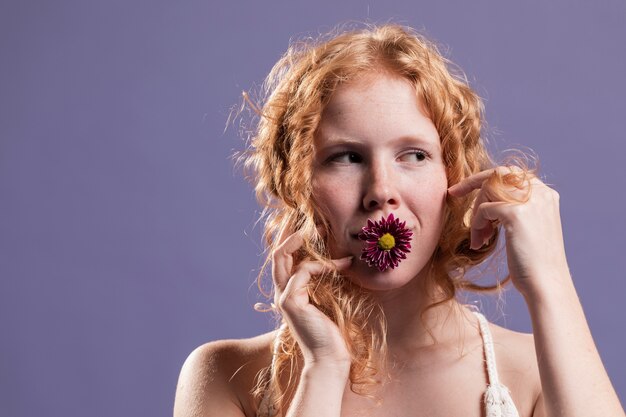 Front view of redhead woman posing with a chrysanthemum on her mouth and copy space