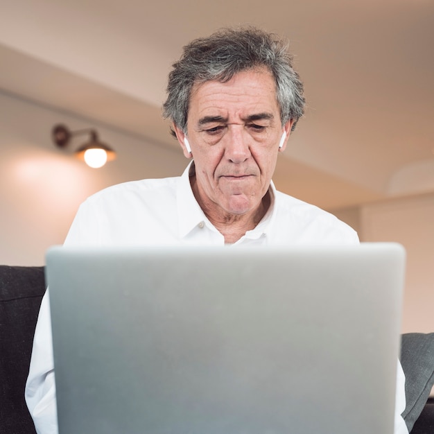 Free photo front view of senior man using laptop with bluetooth earphone on his ears