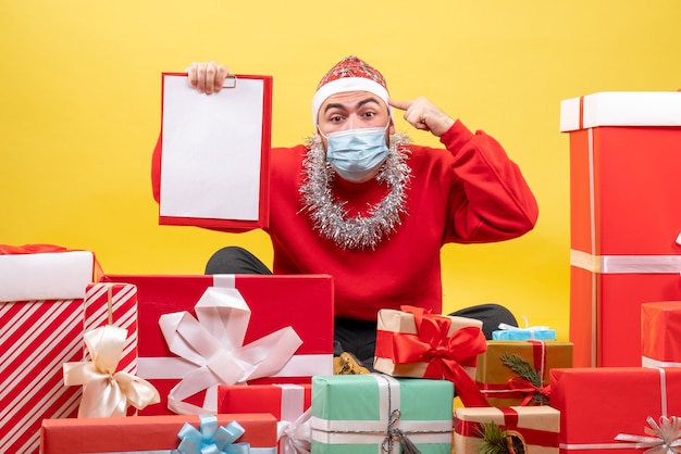 Free photo front view young male sitting around christmas presents on yellow background