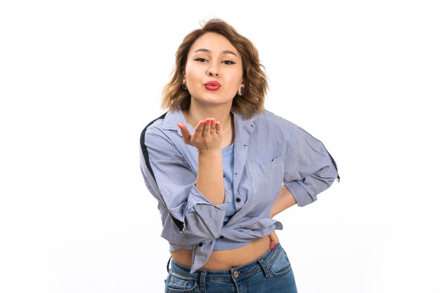 A front view young beautiful girl in blue shirt and blue jeans sending air kisses on the white