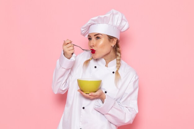 Бесплатное фото Вид спереди молодая женщина-повар в белом костюме повара позирует, держа зеленую тарелку на розовом пространстве, повар кухня работа работа фото