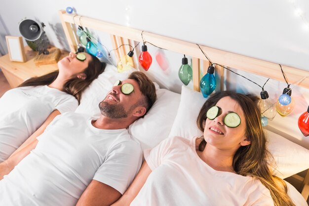 Free photo friends with cucumber slice over eyes laying on decorated bed