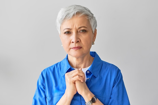 Free photo frustrated worried mature gray haired female holding hands on her chest, having uneasy facial expression, worrying about her husband who is sick. human emotions, reactions and body language