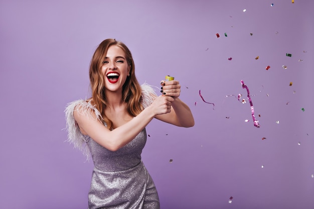 Бесплатное фото Великолепная дама в серебряном платье бросает конфетти на фиолетовую стену