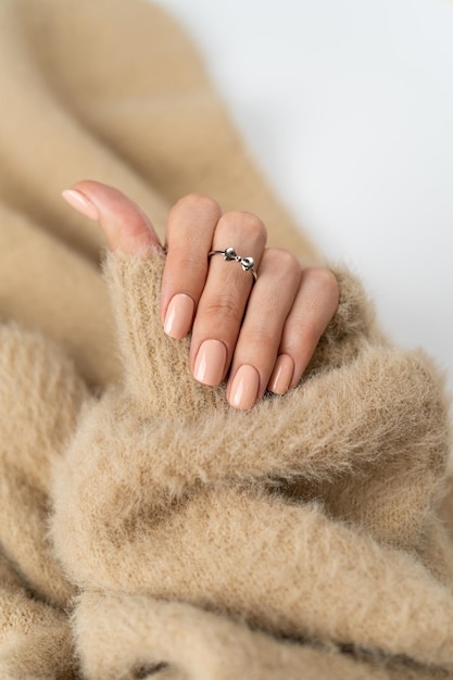 Free photo graceful thin fingers of a girl with a trendy pastel nude manicure and a fluffy soft sweater and a cute silver ring bow