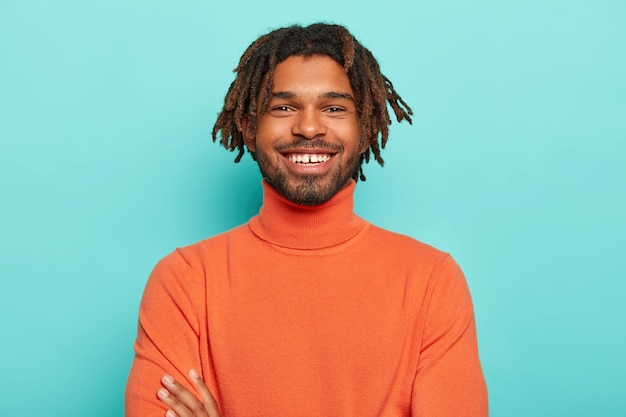 Free photo handsome hipster with dreads has pleasant smile, has white teeth, happy to hear good news, wears bright clothes