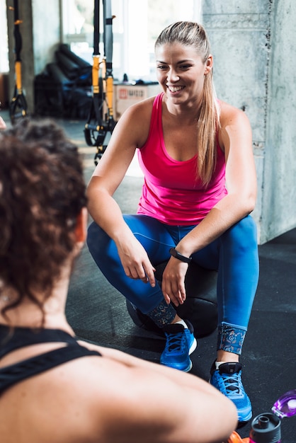 Free photo happy young woman sitting near her friend in gym