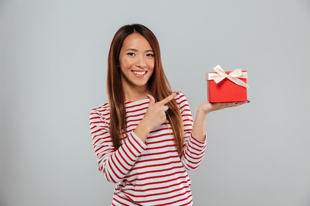 Счастливое молодое азиатское положение дамы изолировало держать подарок и указывать.