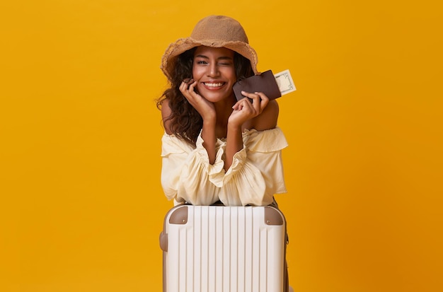 Free photo happy african woman sitting with suitcase isolated on yellow background