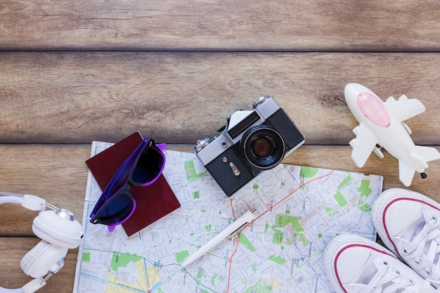 Бесплатное фото Высокий угол обзора наушников; паспорт; солнцезащитные очки; карта; ручка; камера; обувь и самолет на деревянном фоне